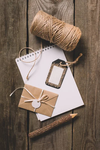 Vista dall'alto del libro di testo vuoto, matita albero, tag, lettera avvolta e stringa beige su sfondo di legno — Foto stock