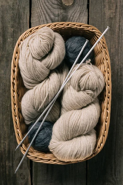 Top view of beige and grey knitting yarn wit knitting needles in wicker basket on wooden background — Stock Photo