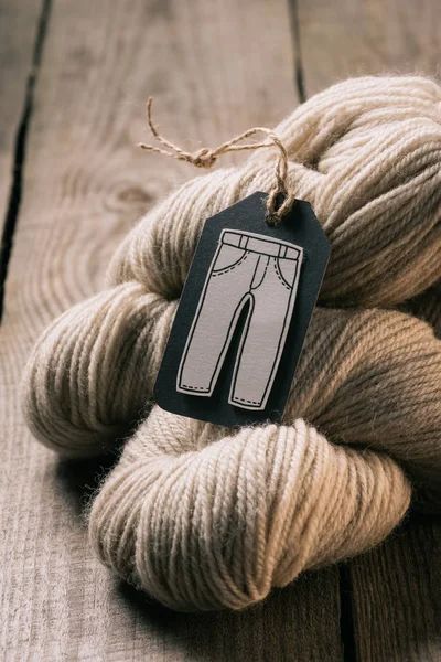 Selective focus of beige yarn ball and tag with trousers on wooden background — Stock Photo