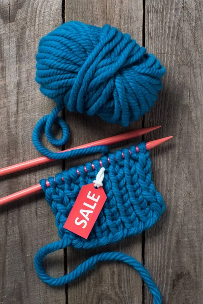 Vue du dessus des aiguilles à tricoter bleues, boule de fil bleu et étiquette de vente sur fond en bois — Photo de stock