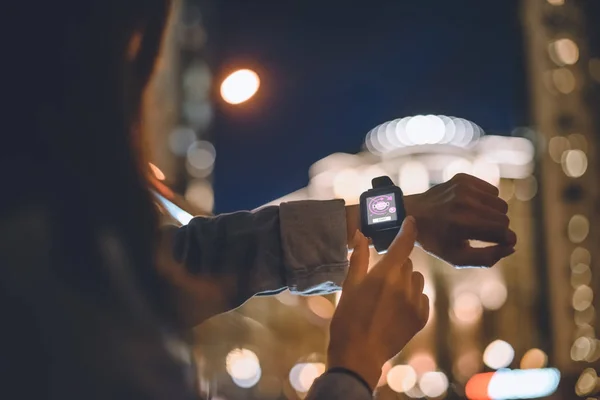 Vue partielle de la femme avec smartwatch sur le poignet et la nuit lumières de la ville sur fond — Photo de stock
