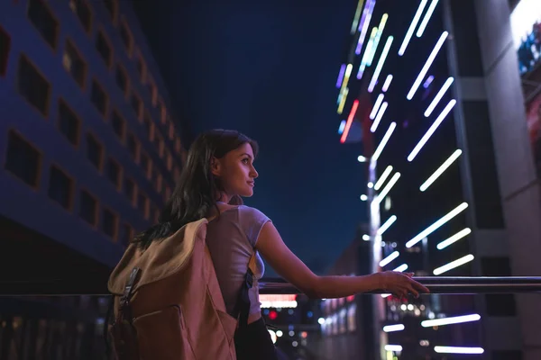 Hermosa mujer pensativa con mochila mirando hacia otro lado en la calle de la ciudad por la noche — Stock Photo