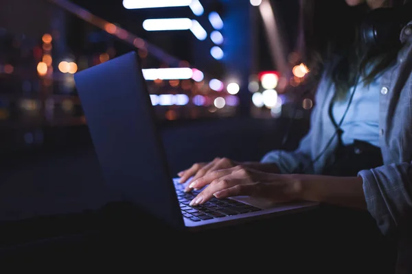 Обрізаний знімок жінки з навушниками, що друкуються на ноутбуці на міській вулиці вночі — стокове фото