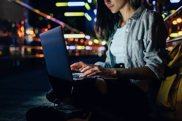 Cropped shot of woman using laptop on street with night city lights on background — Stock Photo
