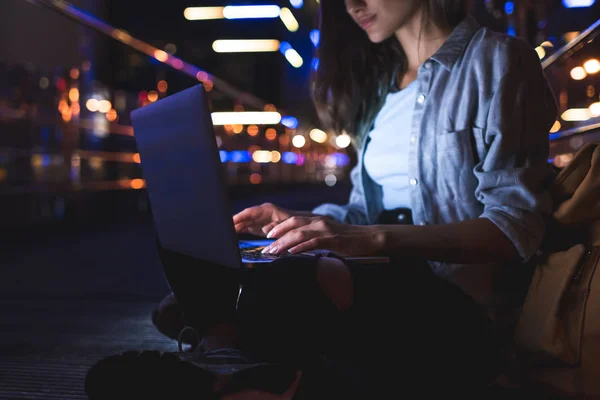 Partial view of woman using laptop on street with night city lights on background — Stock Photo