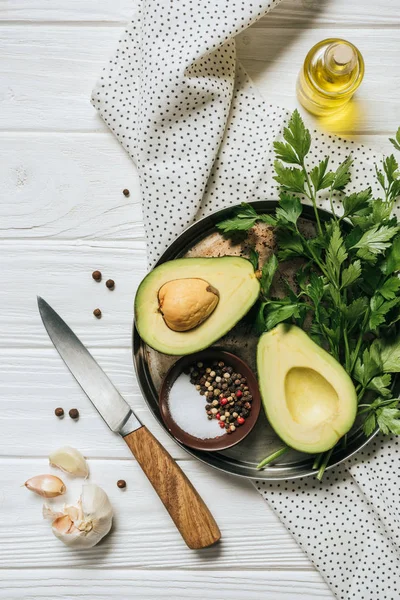 Vista dall'alto di avocado maturo, prezzemolo e ciotola con pepe su vassoio — Foto stock