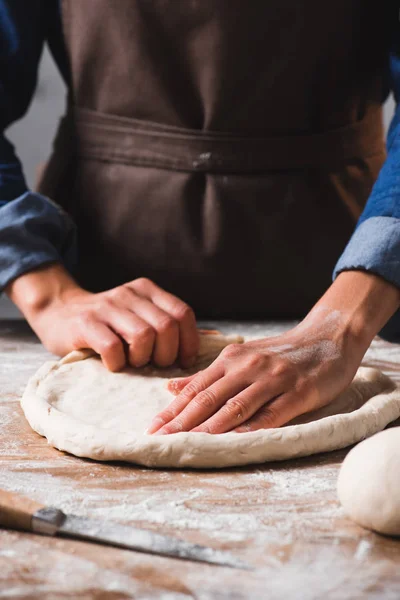 Vue partielle de la femme dans tablier pétrissant pâte pour pizza — Photo de stock