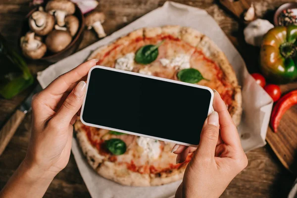 Foto recortada de bloguero de alimentos tomando fotos de pizza cocida en papel de hornear en la superficie de madera - foto de stock