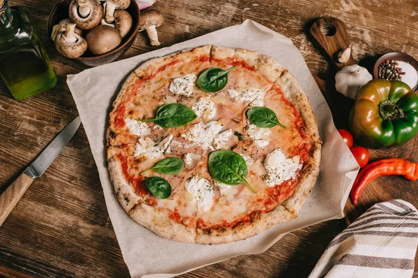Vista superior de la pizza italiana, ingredientes y cuchillo en la mesa de madera - foto de stock