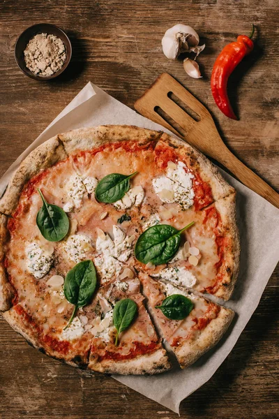 Top view of italian pizza, garlic, chili pepper and wooden spatula on wooden tabletop — Stock Photo