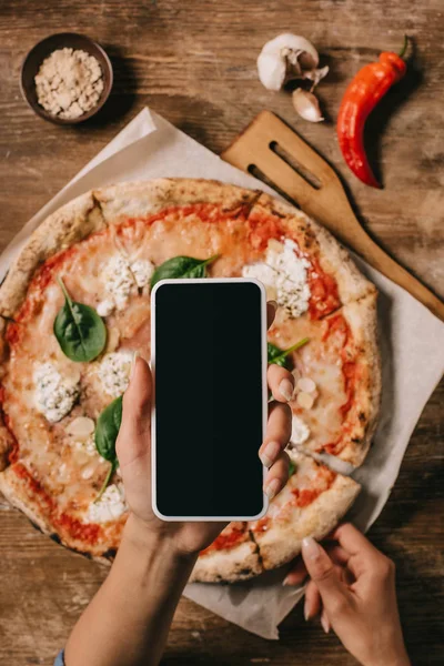 Colpo ritagliato di food blogger scattare foto di pizza cotta su carta da forno su superficie di legno — Foto stock