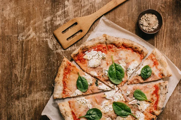 Draufsicht auf geschnittene italienische Pizza und Holzspatel auf hölzerner Tischplatte — Stockfoto