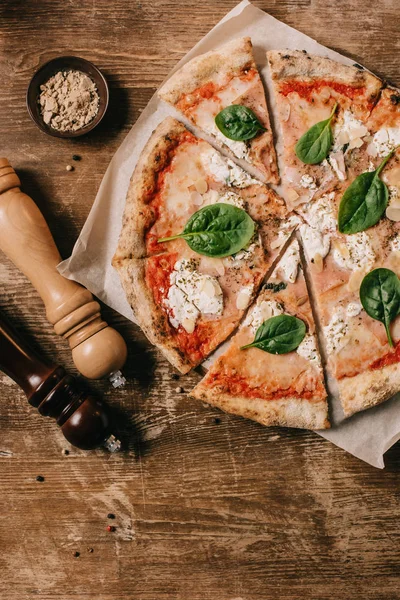 Vista superior de la pizza italiana cortada, molinillos de sal y pimienta en la mesa de madera - foto de stock