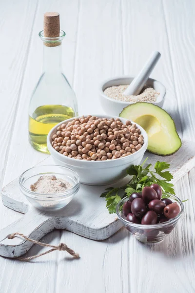 Vista de cerca de garbanzos crudos, especias, perejil y aguacate (ingredientes de hummus) en la mesa de madera - foto de stock