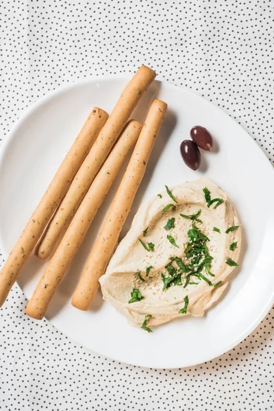 Top view of hummus, breadsticks and olives on plate on linen — Stock Photo