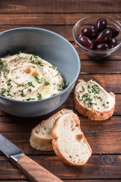Close up view of olives, bread and hummus with parsley and chickpeas in bowl on wooden surface — Stock Photo