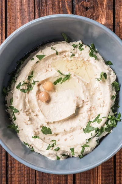 Hummus mit Petersilie und Kichererbsen in Schüssel auf Holztischplatte — Stockfoto