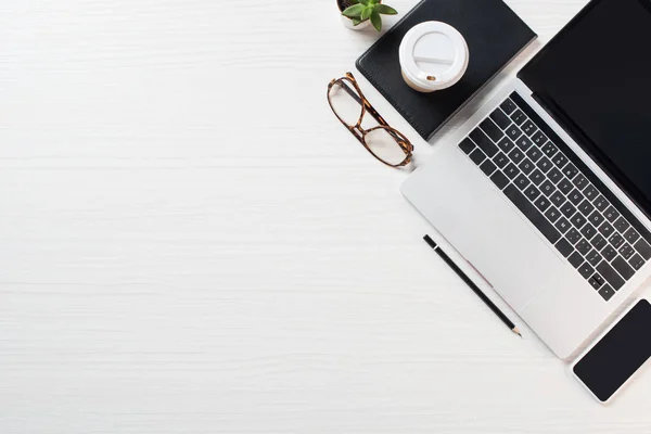 Top view of workplace with eyeglasses, coffee and laptop  with blank screen on table — Stock Photo