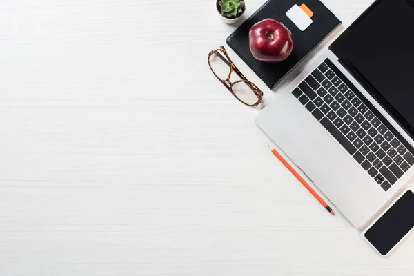 Elevated view of eyeglasses, apple, smartphone and laptop on table — Stock Photo