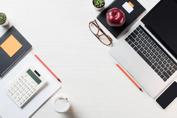 Vista superior del lugar de trabajo con calculadora, papelería, café y dispositivos digitales en la mesa - foto de stock