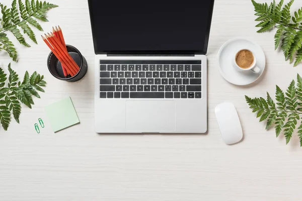 Top view of workplace with laptop, computer mouse, coffee and stationery surrounded by fern leaves — Stock Photo