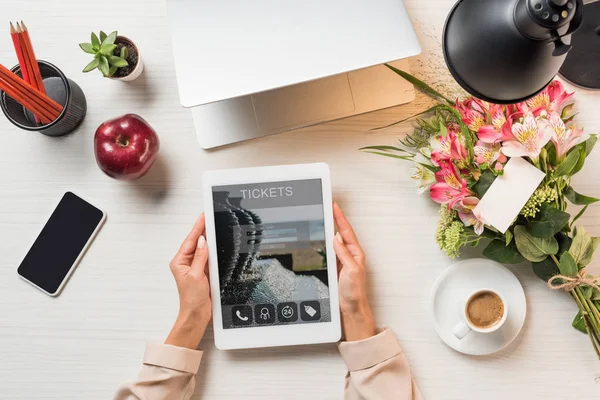 Immagine ritagliata di donna freelance con tablet digitale con biglietti sullo schermo a tavola con tazza di caffè, gadget e fiori con biglietto di auguri — Foto stock