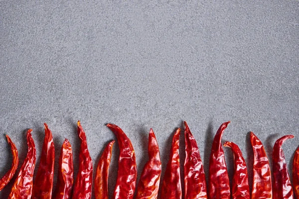 Top view of dried red chili peppers arranged on grey tabletop — Stock Photo