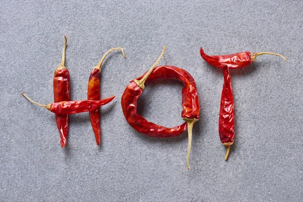 Top view of chili peppers arranged in hot lettering on grey tabletop — Stock Photo
