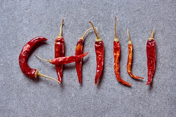 Top view of chili peppers arranged in chilli lettering on grey tabletop — Stock Photo
