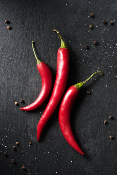 Top view of three red ripe chili peppers on black surface — Stock Photo
