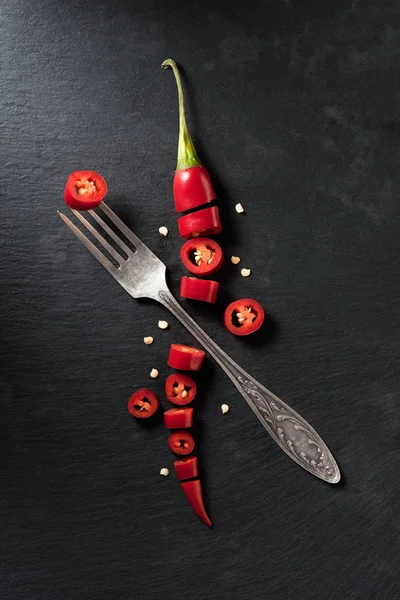 Elevated view of cut red ripe chili pepper and fork on black surface — Stock Photo