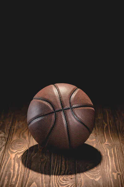 Une balle de basket brune sur le sol en bois dans la chambre noire — Photo de stock