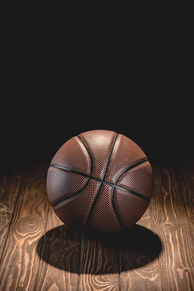 Una pelota de baloncesto de goma en el suelo de madera en habitación oscura - foto de stock