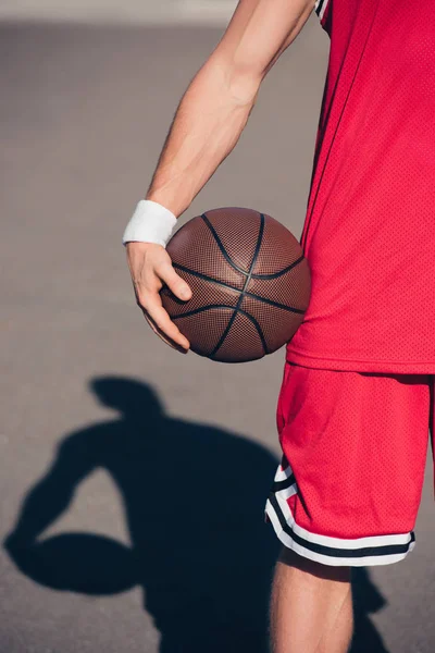 Cropped image of sportsman holding basketball ball on street — Stock Photo