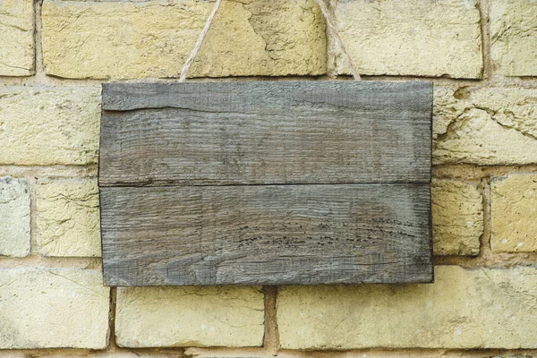 Tablero de madera vacío colgando en la pared de ladrillo - foto de stock