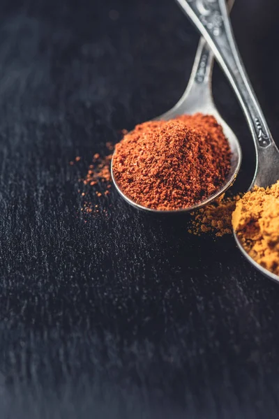 Close-up view of spoons with powdered chili and curry on black background — Stock Photo