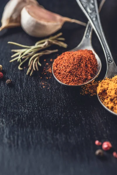 Vista de cerca de cucharas con chile y curry en polvo sobre negro - foto de stock
