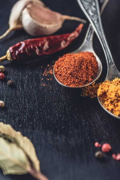 Vue rapprochée des cuillères au chili et curry en poudre sur fond noir — Photo de stock