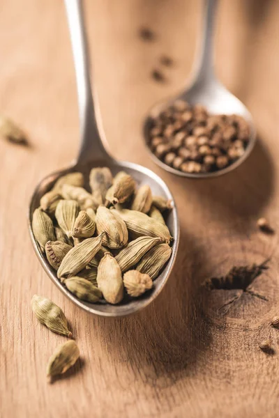 Vue rapprochée des cuillères avec cardamome et graines de coriandre sur la surface en bois — Photo de stock