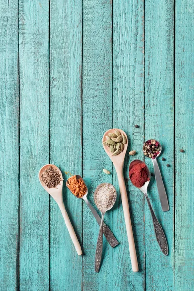 Draufsicht auf Löffel mit verschiedenen getrockneten aromatischen Gewürzen auf türkisfarbener Holzoberfläche — Stockfoto