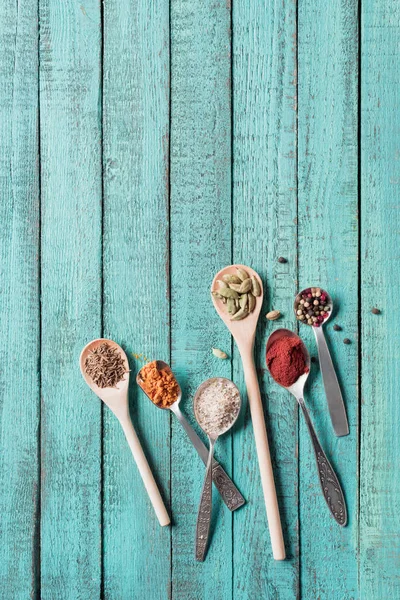 Vue de dessus des cuillères avec diverses épices aromatiques séchées sur une surface en bois turquoise — Photo de stock