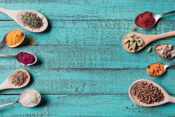 Top view of spoons with various dried seasonings on turquoise wooden surface — Stock Photo