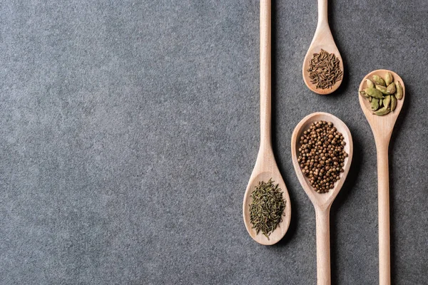 Vue de dessus des cuillères en bois avec assaisonnements aromatiques secs sur fond gris — Photo de stock