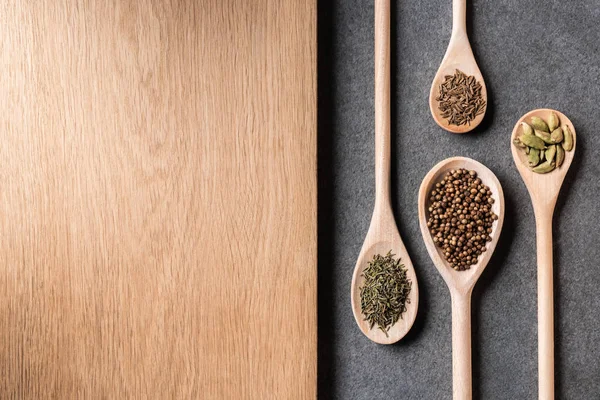 Top view of dried spices on wooden spoons and wooden board on grey background — Stock Photo