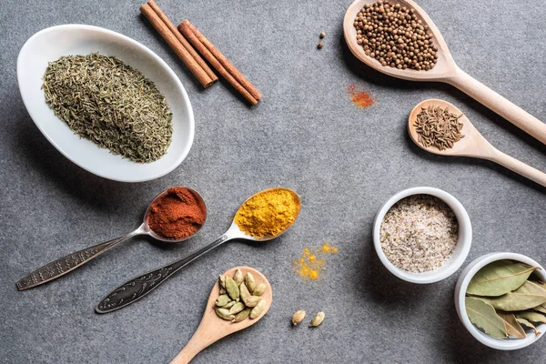 Top view of various aromatic dried seasonings in bowls and spoons on grey surface — Stock Photo