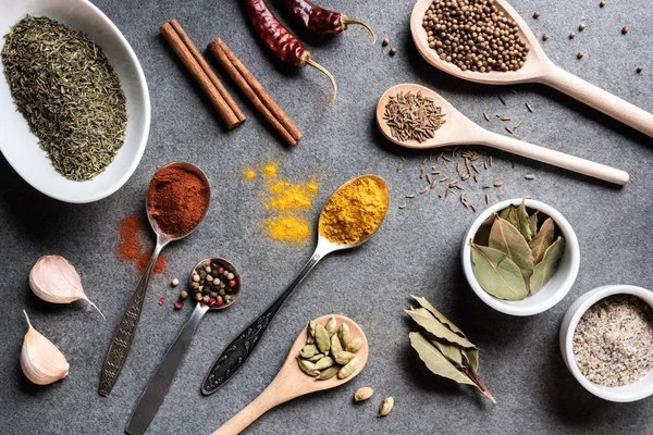 Top view of various aromatic dried spices in bowls and spoons on grey surface — Stock Photo