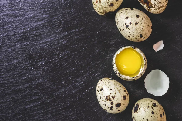 Top view of broken egg and unshelled quail eggs on black background — Stock Photo