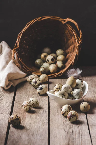 Organic quail eggs in wicker basket and feather on wooden table — Stock Photo