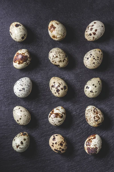 Vue du dessus des œufs de caille non décortiqués biologiques crus sur noir — Photo de stock