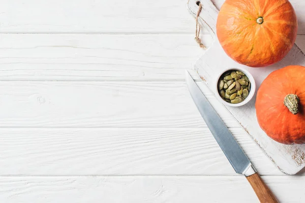 Vue de dessus de la planche en bois avec des citrouilles, couteau et graines de citrouille sur la table — Photo de stock